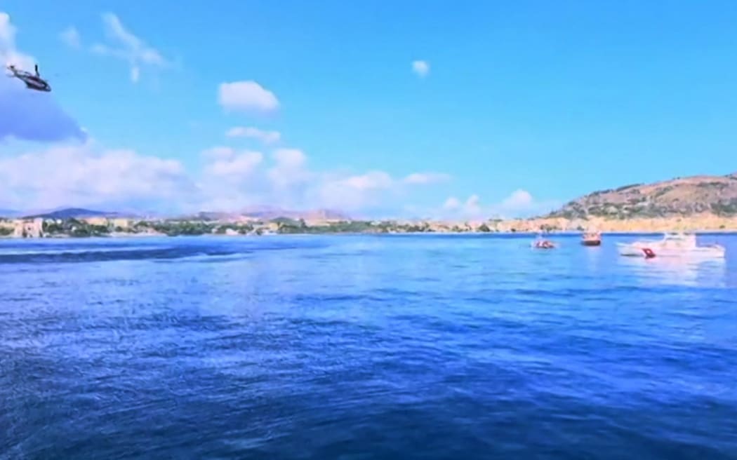 This handout frame grab taken and released from a video footage provided by Italian Coastguard, shows a Coast Guard boat with Italian fireboats and an Italian fire brigade helicopter search for six others missing after recovering a victim due to a sailboat sank off the coast of Porticello, nosthwestern of Sicily Island, on August 19, 2024. One person was killed and rescuers were searching for six others missing after a luxury superyacht called "The Bayesian" with 22 people aboard majority of those were British, sank during a sudden storm off the coast of Italy's Sicily, officials said, on August 19, 2024. (Photo by Handout / ITALIAN COASTGUARD / AFP) / RESTRICTED TO EDITORIAL USE - MANDATORY CREDIT "AFP PHOTO / Italian Coastguard " - NO MARKETING NO ADVERTISING CAMPAIGNS - DISTRIBUTED AS A SERVICE TO CLIENTS