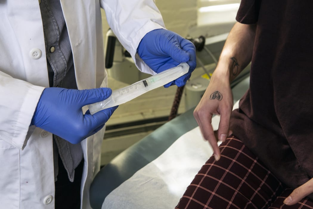 A doctor showing a patient a syringe used to inject testosterone. Guidelines:: https://genderspectrum.vice.com/guidelines