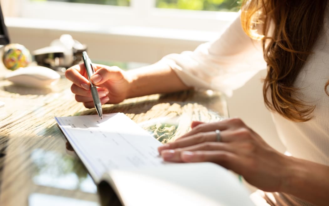 Businesswoman's Hand Signing Cheque On Wooden Desk