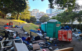 A large pile of tents and chairs with some portaloos in the background.