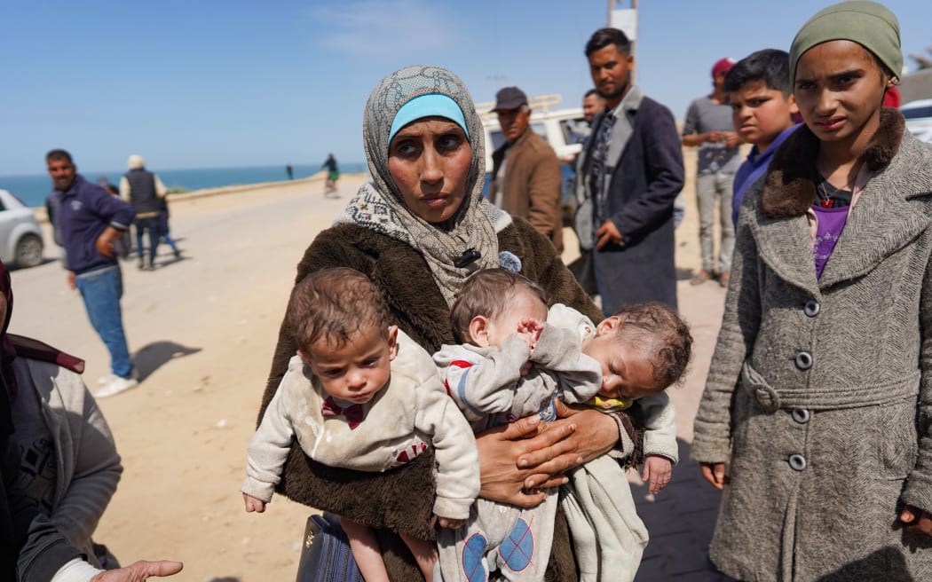 A woman carries three babies as she reaches the central part of the Gaza Strip after fleeing the Al-Shifa hospital compound in Gaza City, on March 21, 2024. Israel's army was on March 21 four days into a raid at Al-Shifa, Gaza's largest hospital, where the military says Hamas was operating from among patients and displaced civilians. (Photo by AFP)