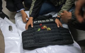 Family members and colleagues touch the bulletproof vest laid on the body of one of the Palestinian journalists killed in an Israeli strike, before the funeral in Khan Yunis, in the southern Gaza Strip on January 22, 2026.