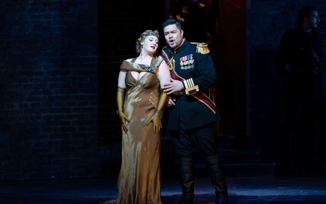 Pene stands on stage dressed in military regalia. He clutches the arm of a woman in a golden gown, and sings sweetly as she swoons.