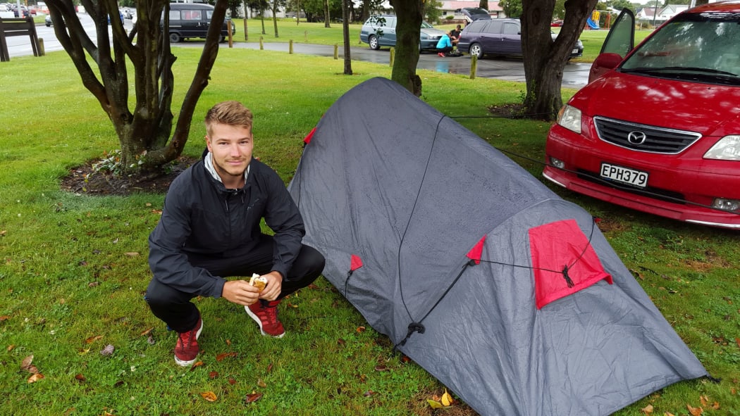 Freedom camper Malte Kellermann crouches next to his tent near Addington Park in Christchurch.