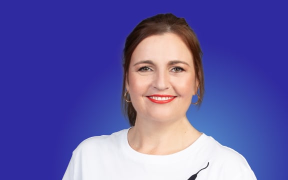 Charlotte Ryan smiles wearing bright red lipstick and a Kate Sylvester T-shirt. Bright blue background.