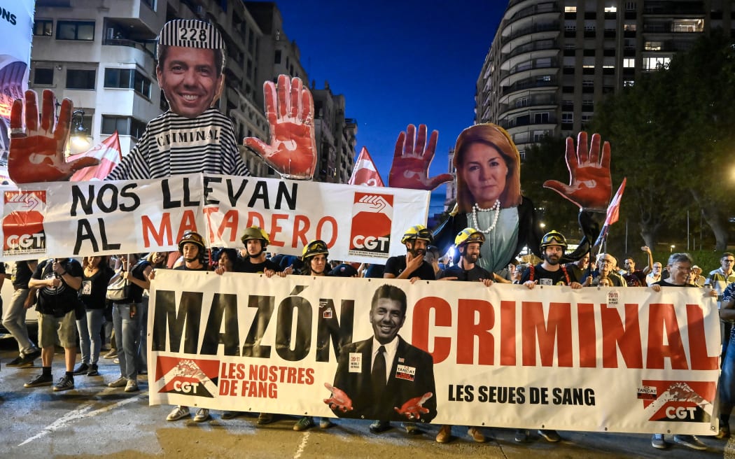 Demonstrators hold up banners depicting the regional President Carlos Mazon and vice-president Susana Camarero (R) during a protest march to mark the first anniversary of last year's deadly floods and demand accountability in Valencia on October 25, 2025. The protest comes nearly one year since torrential rain on October 29, 2024  caused flooding in towns near Valencia, killing 229 people, Spain's deadliest natural disaster in decades. (Photo by Jose JORDAN / AFP)