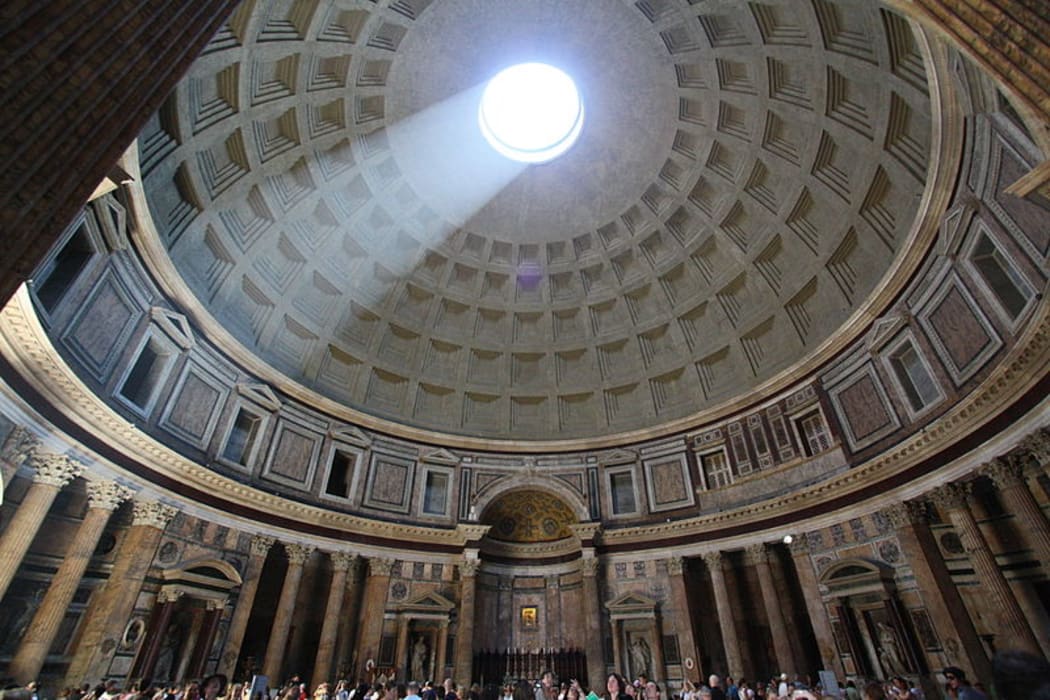 The inside of the Pantheon with light shining down from the Oculus on to tourists standing beneath