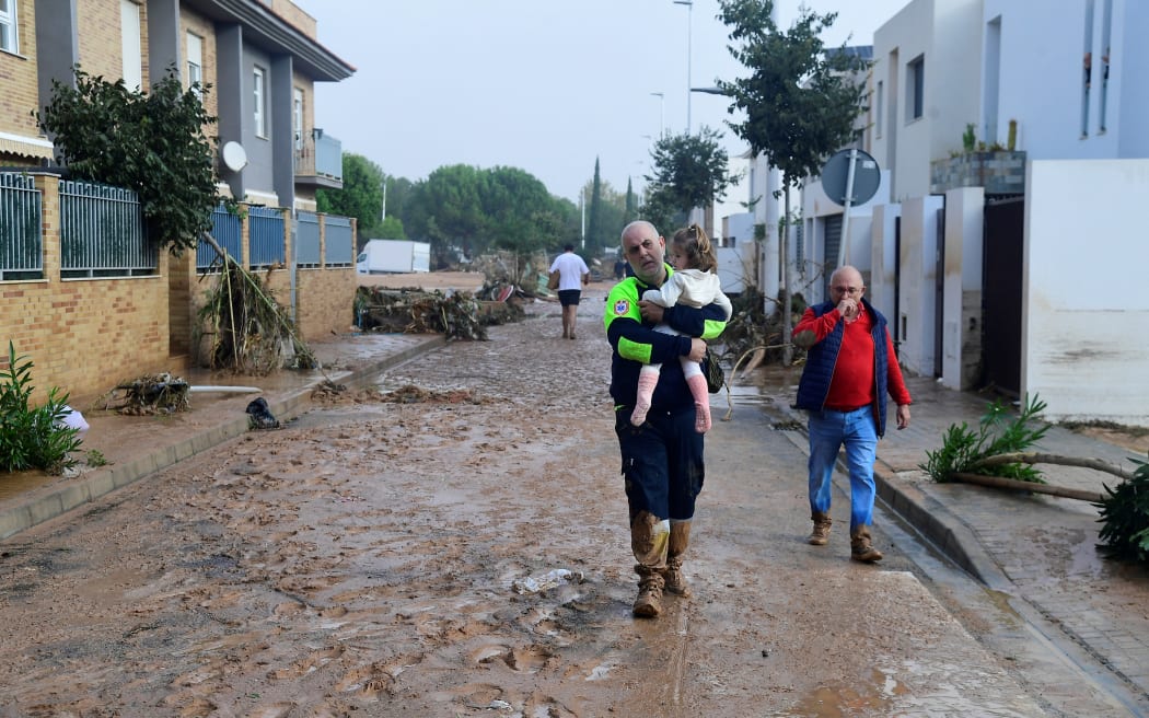 A Civil Protection member carries a child in a street covered in mud in a flooded area in Picanya, near Valencia, eastern Spain, on October 30, 2024. - Floods triggered by torrential rains in Spain's eastern Valencia region has left 51 people dead, rescue services said on October 30. (Photo by Jose Jordan / AFP)