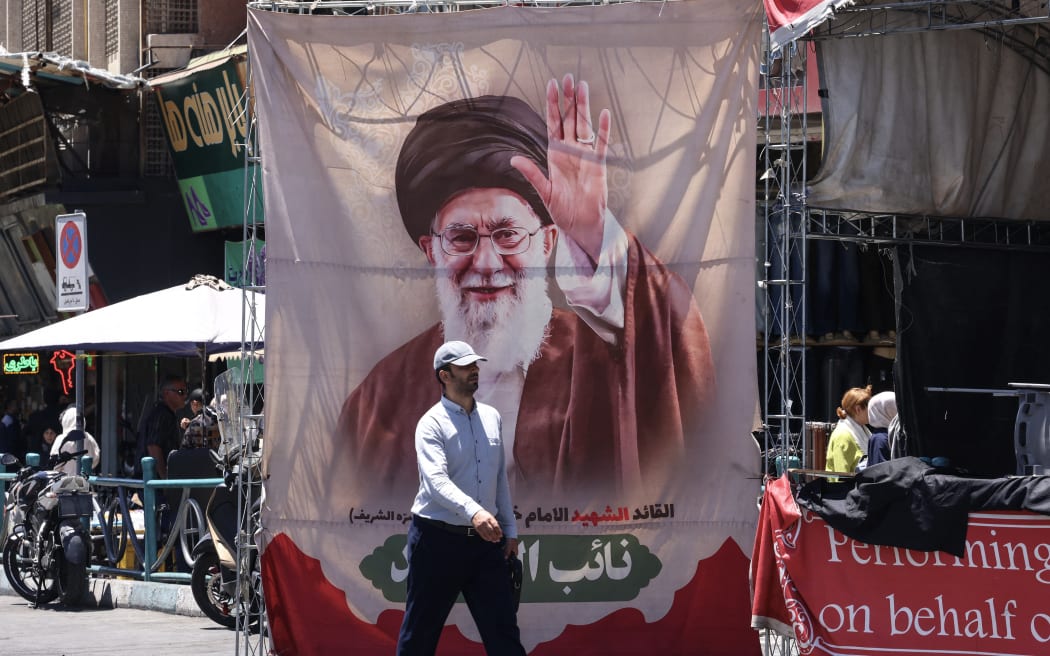 An Iranian man walks past a banner depicting slain supreme leader Ayatollah Ali Khamenei at Valiasr Square in Tehran on June 15, 2026. The United States and Iran agreed a peace deal and an “immediate and permanent” end to military operations on all fronts including Lebanon, mediator Pakistan said, signaling the apparent end to more than three months of war in Middle East. (Photo by ATTA KENARE / AFP) /