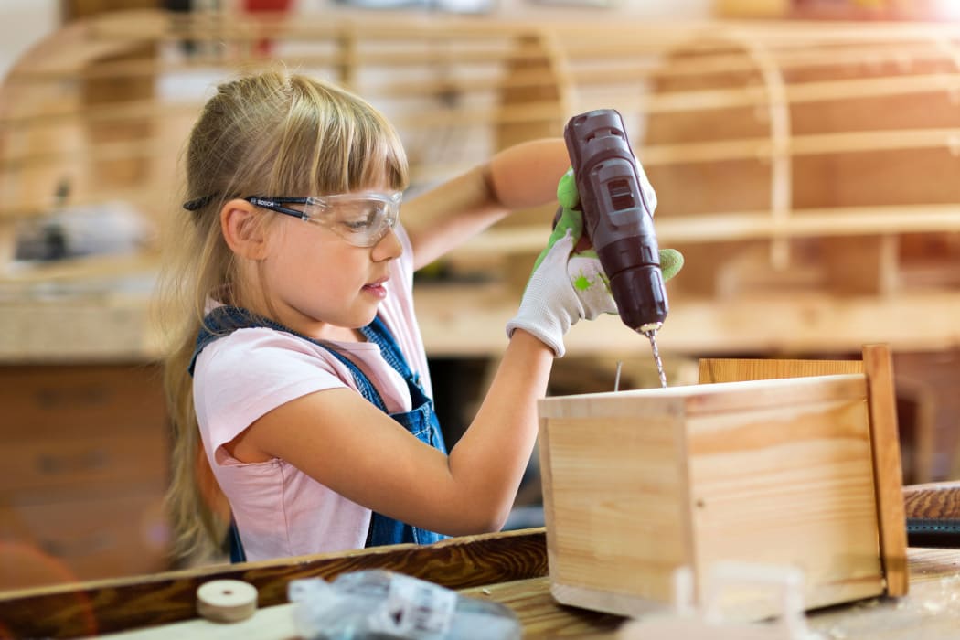 A photo of a young girl using a drill in wood working class