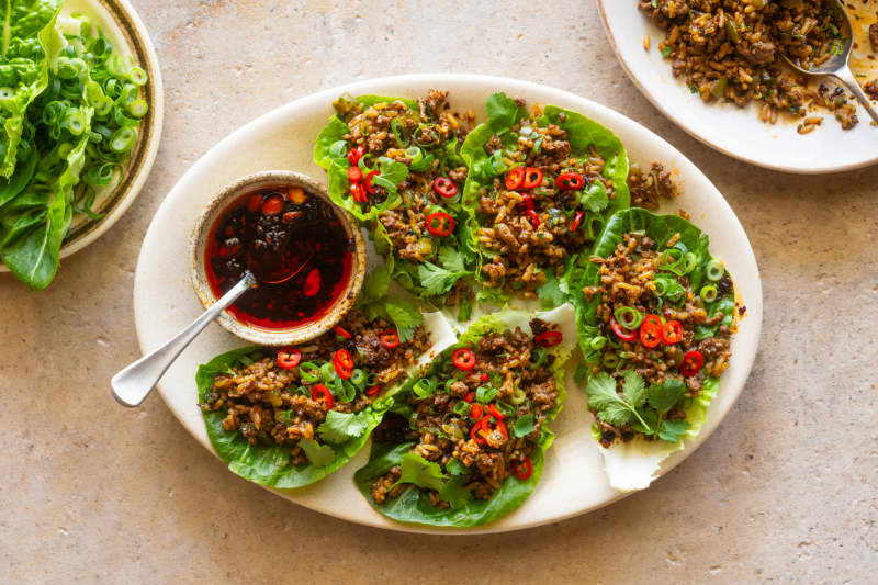A platter showing lettuce leaf cups filled with spicy cumin lamb fried rice, garnished with sliced chilli.