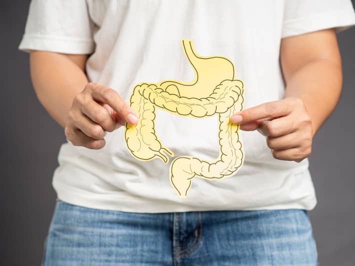 Hand holding a large intestine shape made from yellow paper while standing over a gray background.