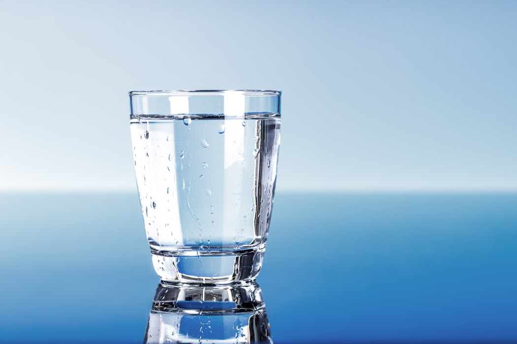 A close-up of a glass of drinking water, on a blue background