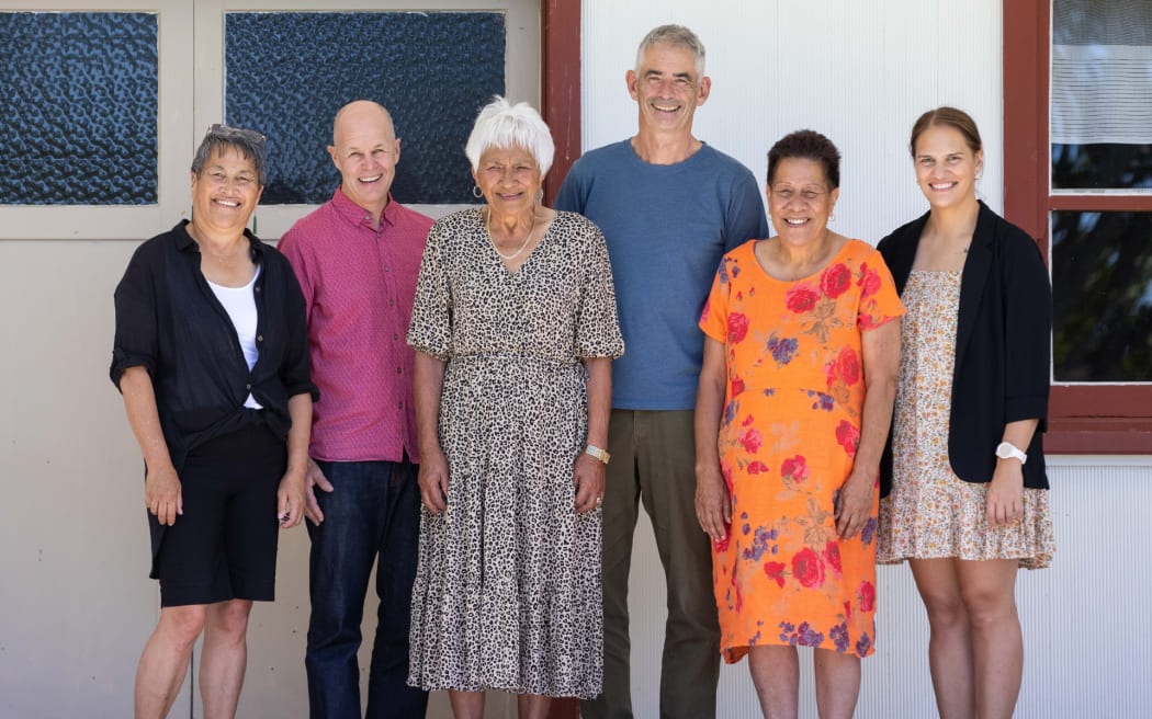 A group of six people gathered in front of a white building. They are smiling at the camera.