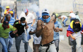 Demonstrators run from tear gas fired by Bolivarian National Guard officers during clashes in Urena, Venezuela, near the border with Colombia, Saturday, Feb. 23, 2019.