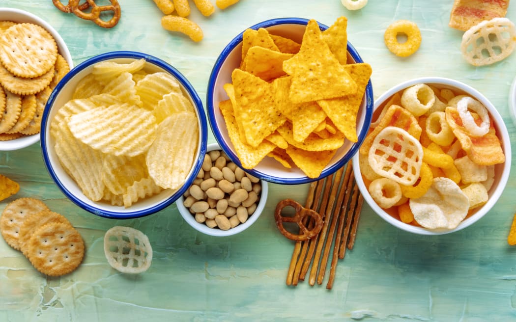 Potato and tortilla chips and other salty snacks, shot from above with copy space. Party food on a teal blue background. A mix of appetizers in bowls