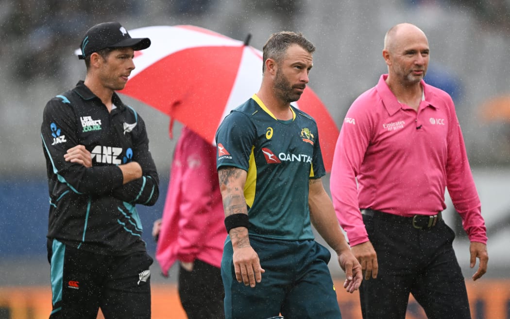 Australian captain Matthew Wade and New Zealand captain Mitch Santner with umpire Wayne Knights during a break in play due to rain at the 3rd T20 Chappell-Hadlee cricket international at Eden Park.