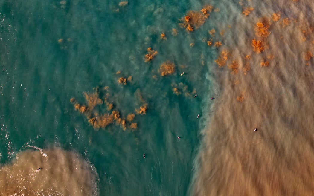 A drone shot above coastal water showing clear blue water on one side and brown, sediment-laden water to the right