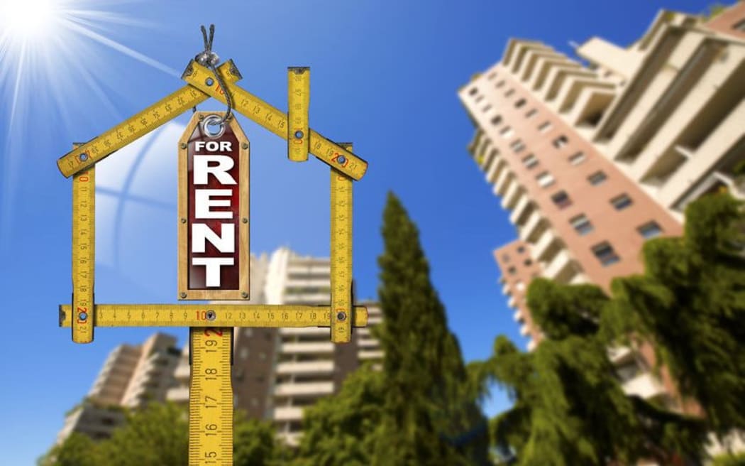 For rent sign inside ruler in shape of house, with high rise building in background.