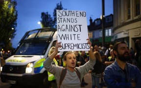 A person holds a placard reading 'Southend stands against white Supremacists' during a counter demonstration to an anti-immigration protest called by far-right activists, near an Immigration Solicitors' office in Westcliff, near Southend-on-Sea, eastern England on August 7, 2024. Thousands of riot police stood ready Wednesday as Britain remained on alert for disturbances during far-right protests across the country. Nightly riots, during which mosques and migrant targets have been attacked, erupted after three children were murdered in Southport on July 29. (Photo by AFP)