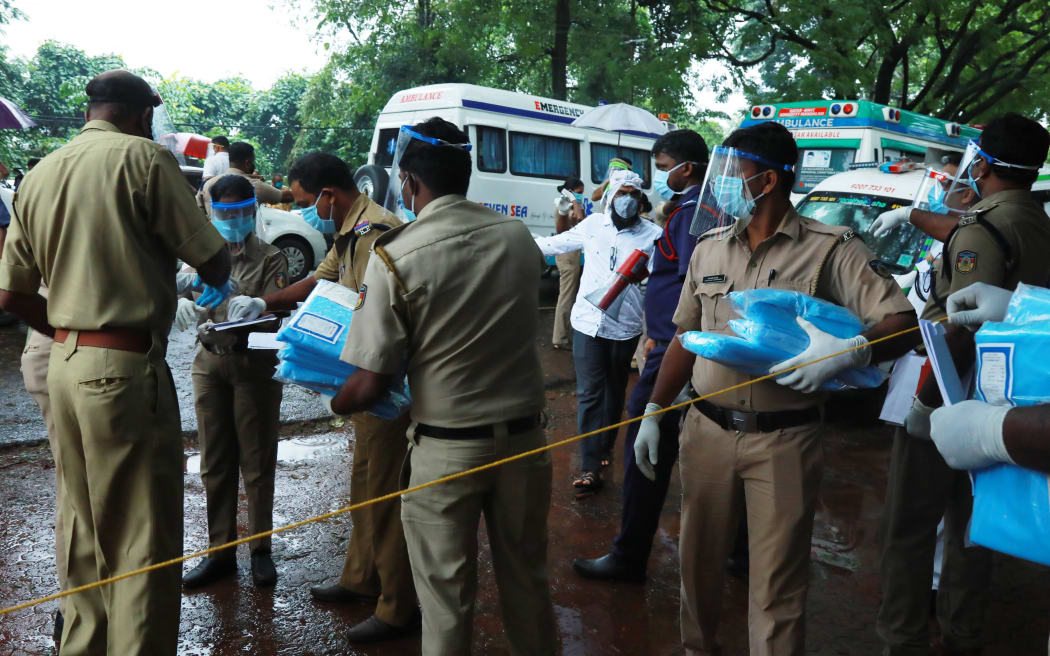 Police personnel distribute Personal Protective Equipment (PPE) kits amongst each other outside the medical college where Air India Express jet crash victims are taken for the post-mortem examination in Kozhikode, Kerala, on August 8, 2020.
