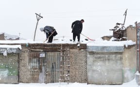 Afghan shopkeepers shovel snow from the roof of their shop during snowfall in Kabul on February 5, 2017.