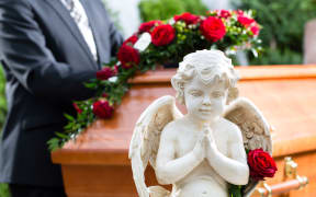 Mourning man on funeral with red rose standing at casket or coffin