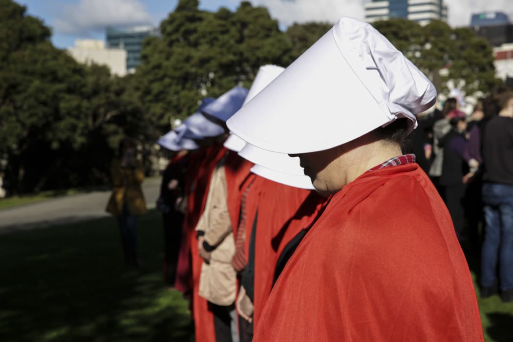 About a dozen handmaidens counter-protesters arrive and line up at the protest.