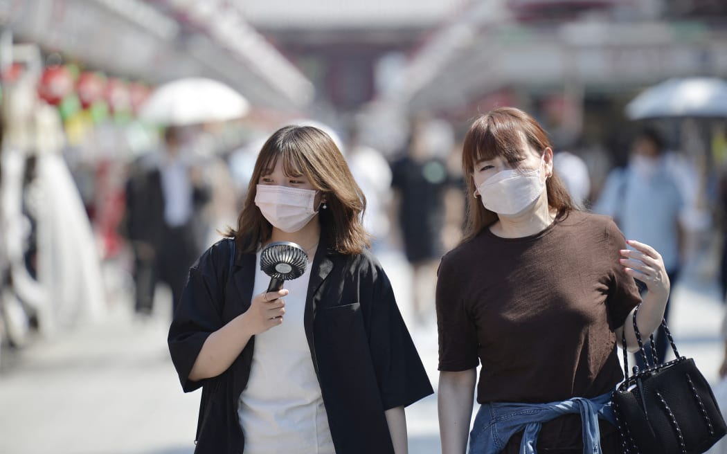 Two women, using portable fan, walk on a street leading to Sensoji Temple in Tokyo under the hot and burning midday sun.