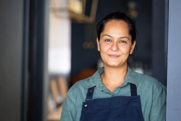 A slightly smiling woman with black hair and a blue apron.