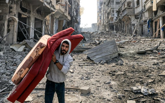 A man walks with mattresses through destruction in the Gaza Strip's Jabalia refugee camp on October 11, 2023, following overnight Israeli airstrikes amid continuing battles between Israel and the Hamas movement. The death toll from five days of ferocious fighting between Hamas and Israel rose sharply overnight as Israel kept up its bombardment of Gaza after recovering the dead from the last communities near the border where Palestinian militants had been holed up. (Photo by MAHMUD HAMS / AFP)