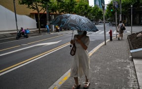 A woman walks on a street protecting herself from the sun with an umbrella in the Jing'an district of Shanghai on July 11, 2022. (Photo by Hector RETAMAL / AFP)