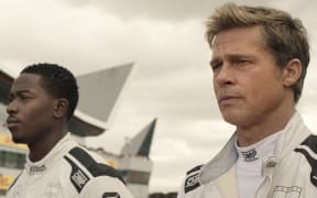 A still from the movie F1: The Movie. Two drivers stare dramatically into the distance wearing specialised white suits.