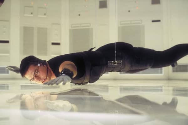 Tom Cruise, wearing tight black clothing, a head set and gloves, hovers above a pane of glass.