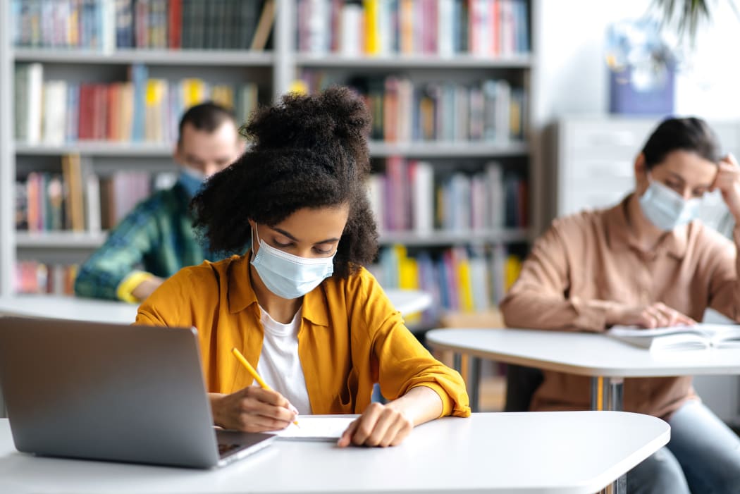 University students taking notes during lecture, wearing masks.
