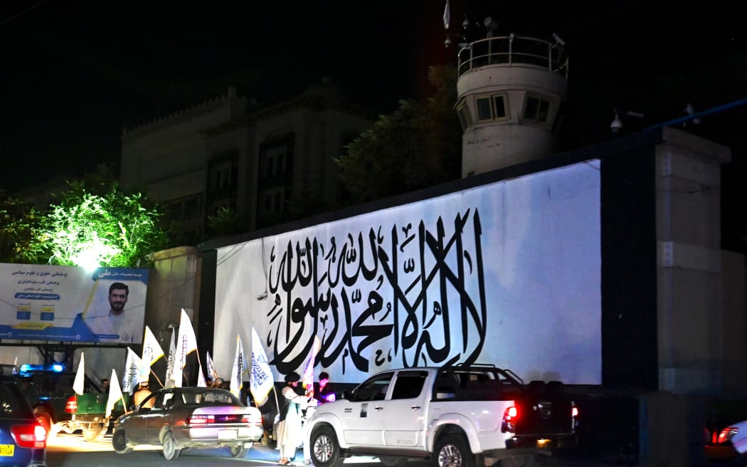 People buy Taliban flags on the eve of the first anniversary of the end of the war with US-led foreign forces, near the US embassy in Kabul on August 30, 2022. (Photo by Wakil Kohsar / AFP)