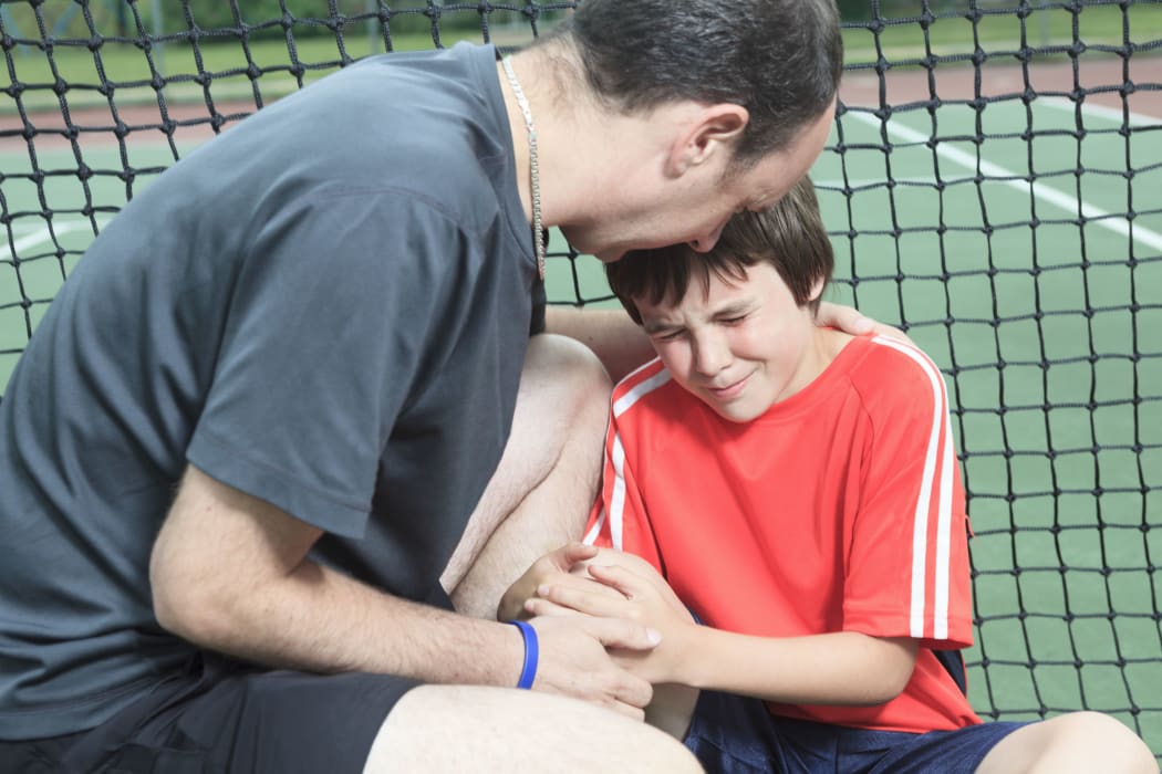 A photo of a father consoling upset boy who has been playing tennis
