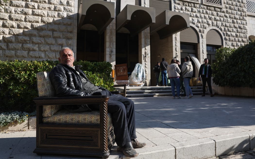 A man sits in an armchair outside of the Tishrin residential palace of Syria's ousted president Bashar al-Assad in Damascus' al-Muhajirin area on December 8, 2024, after Islamist-led rebels declared that they have taken the Syrian capital in a lightning offensive, sending al-Assad fleeing and ending five decades of Baath rule in Syria. (Photo by OMAR HAJ KADOUR / AFP)