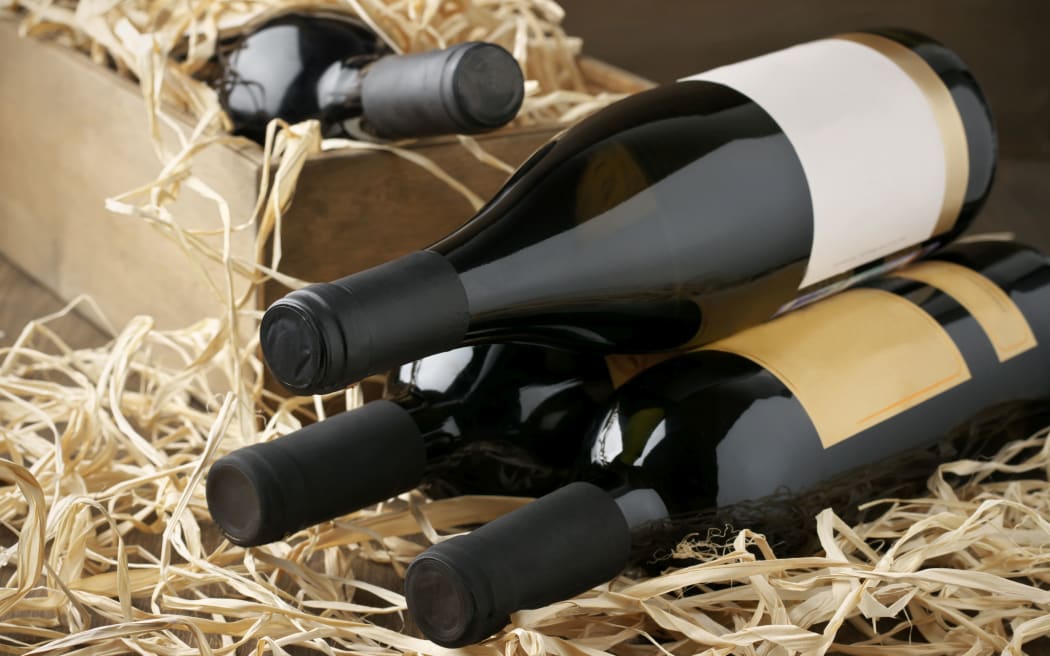 Assorted closed wine bottles lying on straw and vintage wooden box.