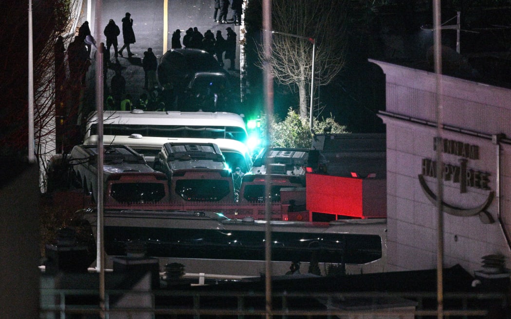 People walk on a road as a person (C) adjusts barbed wire between vehicles blocking the entrance to the compound of the presidential residence of impeached South Korea President Yoon Suk Yeol in Seoul, as seen from a hill, on January 15, 2025. South Korea's Constitutional Court opened the impeachment trial of President Yoon Suk Yeol on January 14 over his failed martial law bid, but quickly adjourned the first hearing after the suspended leader didn't show up. (Photo by ANTHONY WALLACE / AFP)