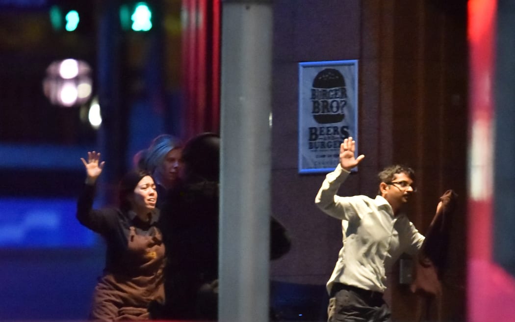 Hostages run out of a cafe in the central business district of Sydney on December 16, 2014. Police stormed the Sydney cafe where a gunman had taken hostages and displayed an Islamic flag, television footage showed early December 16. AFP PHOTO/Peter PARKS (Photo by PETER PARKS / AFP)