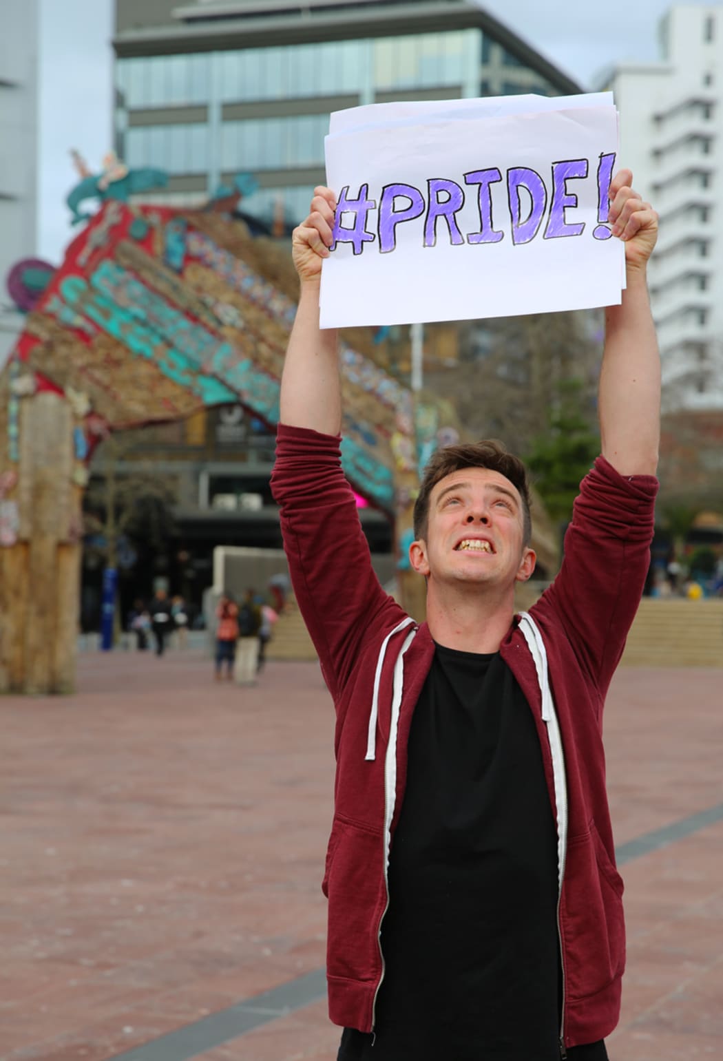 A photo of Eli Matthewson holding up a sign that says "#Pride"