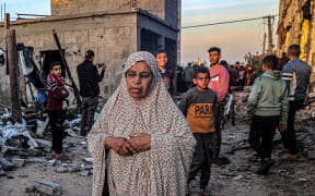 An elderly woman walks past youths near buildings heavily damaged by Israeli bombardment, in Rafah in the southern Gaza Strip on February 11, 2024, amid the ongoing conflict between Israel and the Palestinian militant group Hamas. (Photo by SAID KHATIB / AFP)