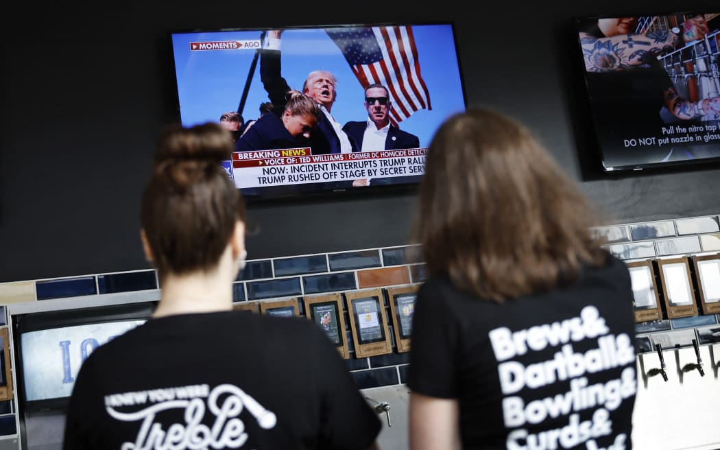 People watch unfolding news at a plaza in Milwaukee, Wisconsin, after shots were fired at a Republican campaign rally as former US president Donald Trump spoke to the crowd, on 13 July, 2024.