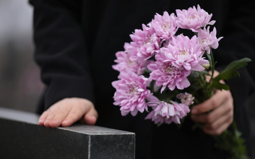 Woman holding chrysanthemum flowers near black granite tombstone outdoors, closeup. Funeral ceremony