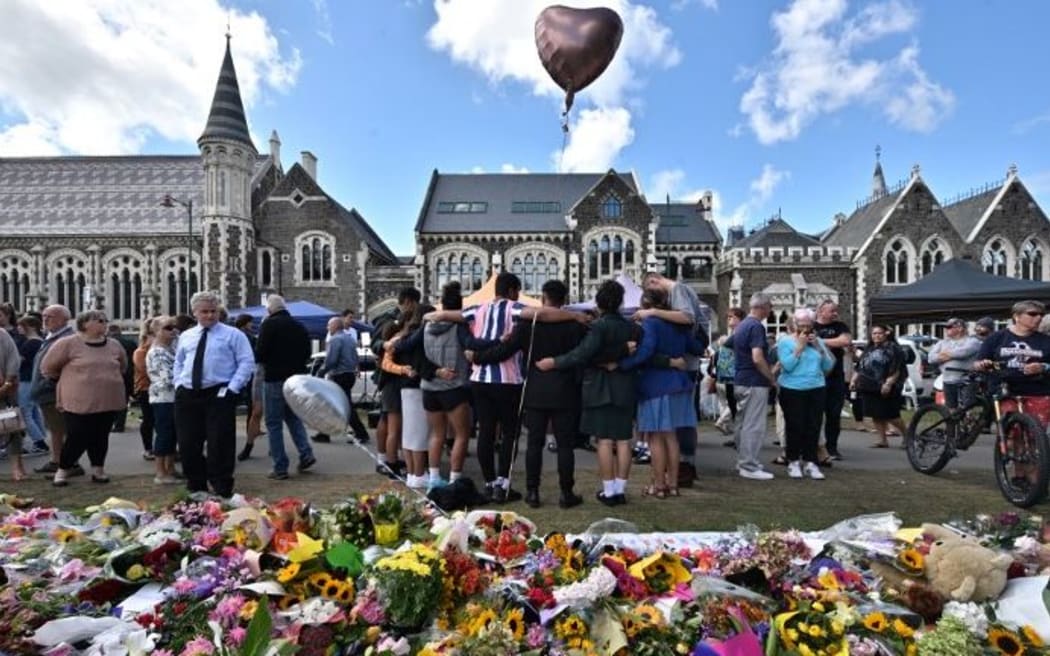 A group of students sing in front of flowers left in tribute to victims of Friday's attacks at the Botanical Garden in Christchurch.