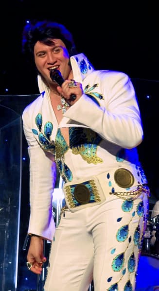 Taurean Kenny Mill holds a microphone as he performs on stage in full Elvis Presley attire.
