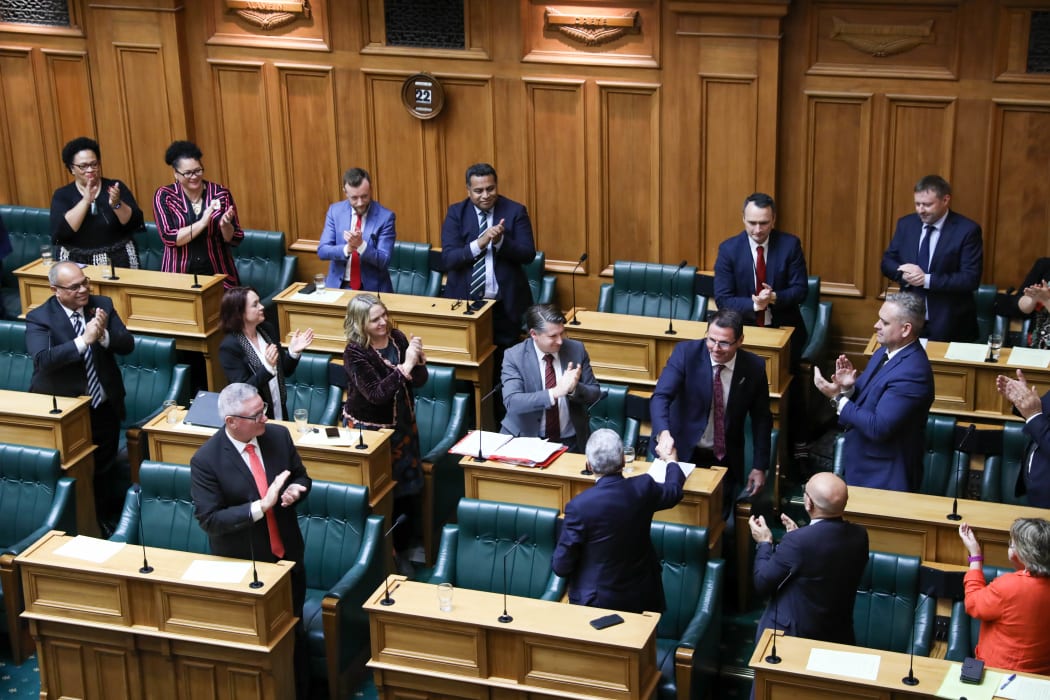 MPs stand to applaud departing New Zealand First MP Clayton Mitchell who shakes his Party Leader Winston Peters hand.
