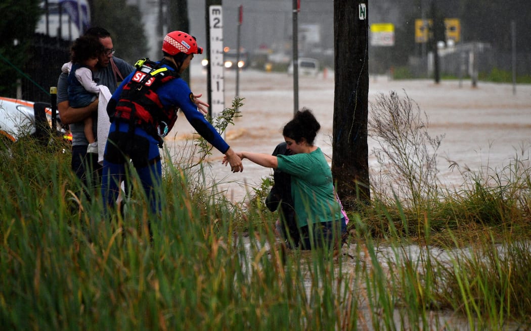 A rescue worker helps residents cross a flooded road during heavy rain in western Sydney on March 20, 2021, amid mass evacuations being ordered in low-lying areas along Australia's east coast as torrential rains caused potentially "life-threatening" floods