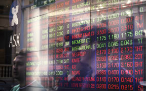 Pedestrians are reflected on a window as they walk past a board displaying stock prices at the Australian Stock Exchange in Sydney.
